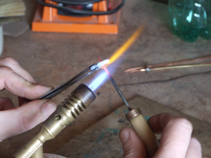 Фото 15. Накаляем иглу и вращая её проплавляем отверстие в стекле. Стекляшку держим близко к факелу.