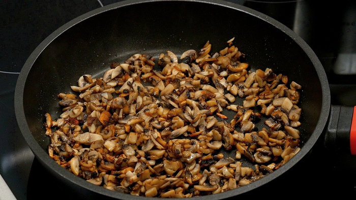 А на соседней конфорке, в сковороде на сильном огне разогреваем растительное или сливочное масло и выгружаем в сковороду нарезанные шампиньоны. Жарим их на сильном огне до тех пор, пока не выпарится лишняя жидкость, и грибы не начнут золотиться.