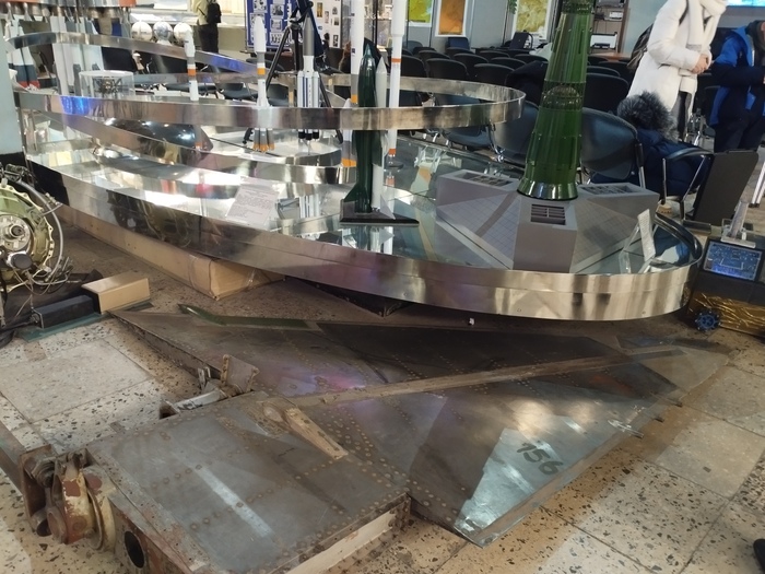 На полу лежит часть оперения из титанового сплава, которая раньше стояла на военной ракете "Буря". Макет ракеты-самолёта стоит чуть позади, по центру снимка, самолёт зелёного цвета.