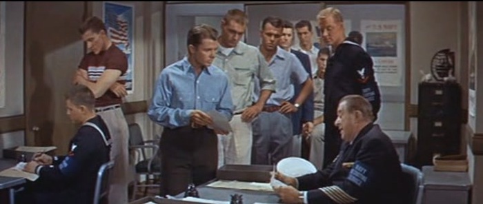 Оди Мёрфи на призывном пункте, кадр из фильма «В ад и назад». Несмотря на прошедшие годы, он по-прежнему сильно проигрывает в габаритах актёрам, играющим призывников